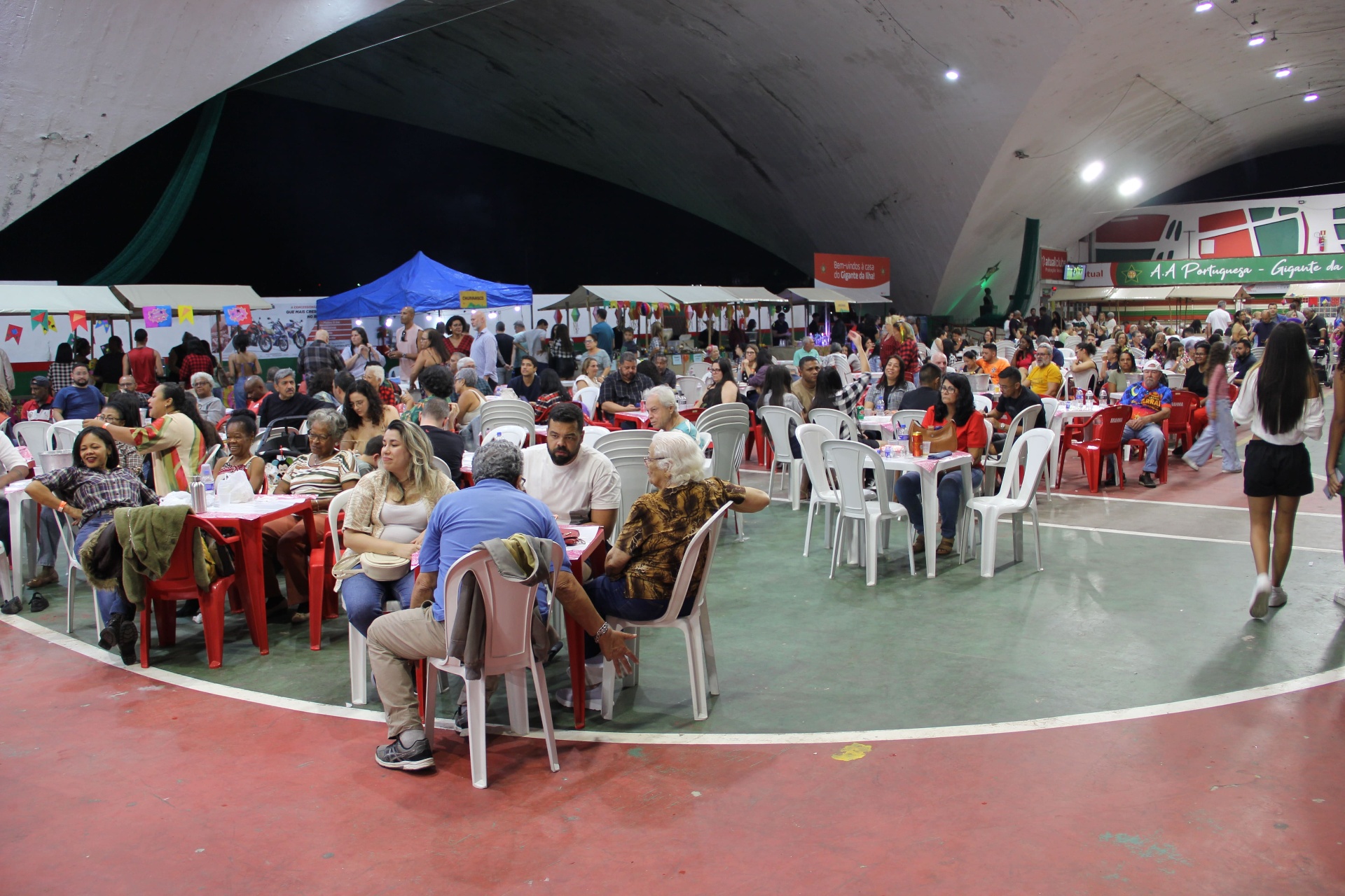 Famílias reunidas nas mesas do salão durante o Arraiá